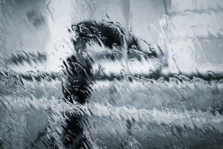 A blurry woman silhouette under the rain with umbrella through wet window. Black and whiteの写真素材