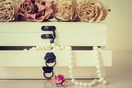 White pearls necklace in wooden casket with faded roses. Toned effectの写真素材