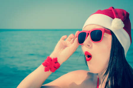Portrait close up of a funny young woman in christmas themed outfit and sunglasses on a beach. Toned effectの写真素材