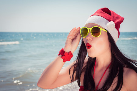 Funny young woman  in Santa Claus hat and sunglasses on a sunny beach. Toned effect