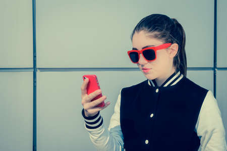 Pretty teenage girl in red sunglasses using her smart phone. Toned effectの写真素材