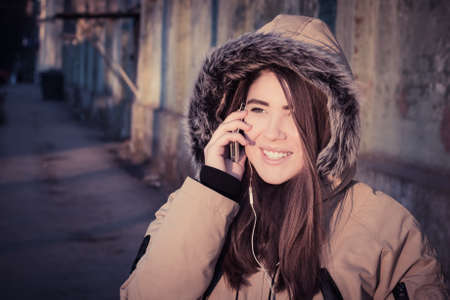 Portrait of a smiling teenage girl wearing winter coat with faux-fur on and talking on her mobile phone. Toned effectの写真素材