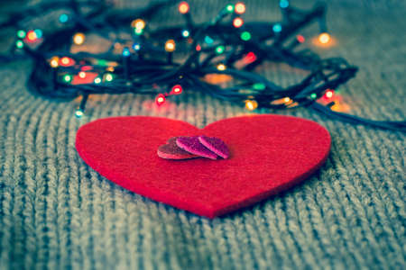 Small decorative hearts on a red felt heart and colorful garland with wool texture in the background. Valentine's day themeの写真素材