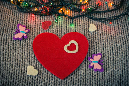 Small white decorative heart on a red felt heart and colorful garland with wool texture in the background. Valentine's day themeの写真素材