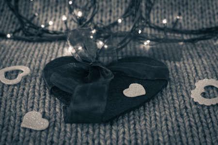 Small white decorative heart on a big felt heart with bow and a garland with wool texture in the background. Black and white. Valentine's day themeの写真素材