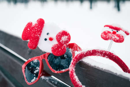 Winter composition with christmas accessories and red sunglasses on a bench covered with snowの写真素材