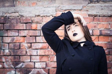 Portrait of a teenage girl with black lipstick posing next to an old brick wall. Toned effectの写真素材