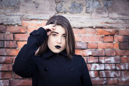Portrait of a teenage girl with black lipstick posing next to an old brick wall. Toned effectの写真素材
