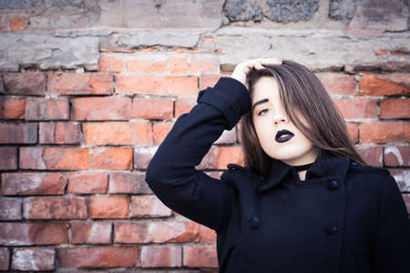Portrait of a teenage girl with black lipstick posing next to an old brick wall. Toned effectの写真素材
