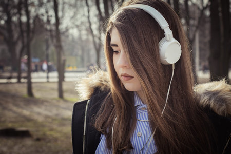 Outdoor close up portrait of a pretty teenage girl with headphones. Toned effect