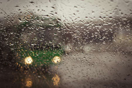Blurry green trolleybus silhouette seen through water drops on the car windshieldの写真素材
