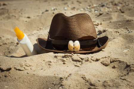Shells and sunglasses on a hat and a bottle of sunscreen lotion lying on the sand. Vacation theme. Toned effectの写真素材
