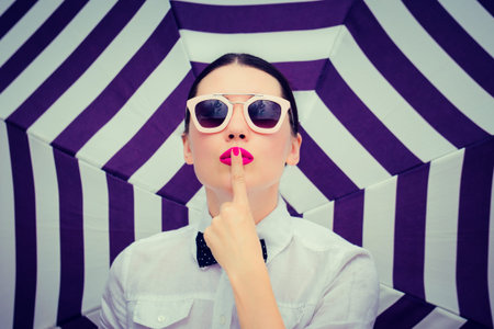 Fashion portrait of a stylish beautiful girl with sunglasses and bright painted lips next to striped...