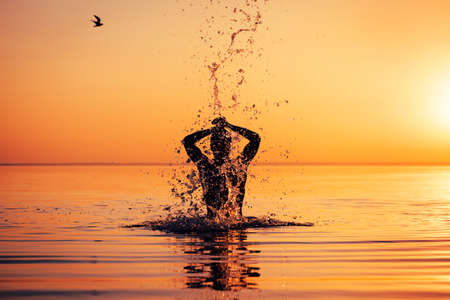 Man's silhouette in calm water at sunset. Man splashing water and enjoying natureの写真素材