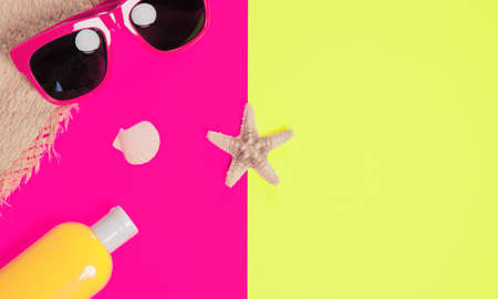 Trendy fashion beach accessories on a bright colorful background. Sunglasses, fragment of a straw hat, a bottle of sunscreen lotion, dried starfish and shells. Summer vacation background.の写真素材