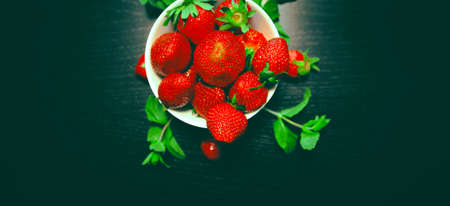 White bowl with fresh red strawberries and mint on a dark wooden table close up. Spring or summer background. Healthy food ingredients theme concept. Image is with copy space.の写真素材
