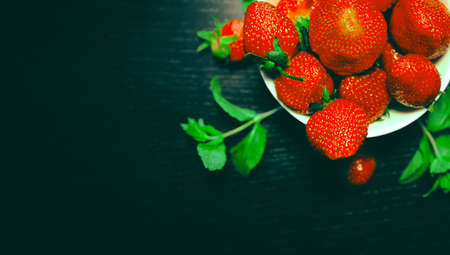 White bowl with fresh red strawberries and mint on a dark wooden table close up. Spring or summer background. Healthy food ingredients theme concept. Image is with copy space.の写真素材