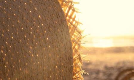 Fragment of a straw hat in sunset light on the beach. Vacation theme concept. Summer holiday backgroundの写真素材