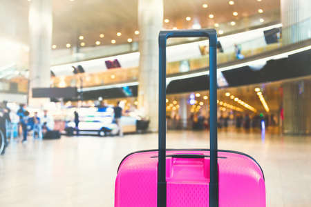 Bright pink suitcase in airport airport terminal waiting area with lounge zone as a background. Traveling luggage in airport terminal. Vacation theme concept. Image is with copy spaceの写真素材