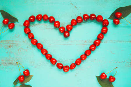 Fresh red cherry in a shape of a heart on an old painted wooden table as a bright colorful summer background for seasonal cards, posters, blogs, web designの写真素材