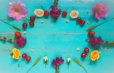 Summer composition with flowers, grass, cherries, strawberries lying as a frame on an old painted...