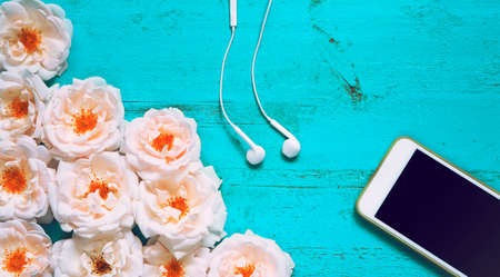 Beautiful summer background with fresh roses, smartphone and white earphones on an old painted wooden table for blogs, web design, posters, seasonal cards and business conceptsの写真素材