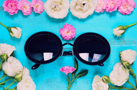 Trandy fashion sunglasses and fresh garden roses on an old painted wooden table. Summer background...