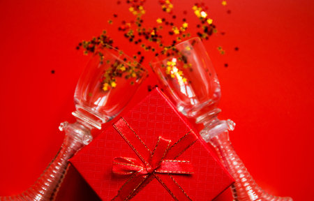 Red gift box, two vintage glasses on red background with decorative metallic stars. Holiday theme...