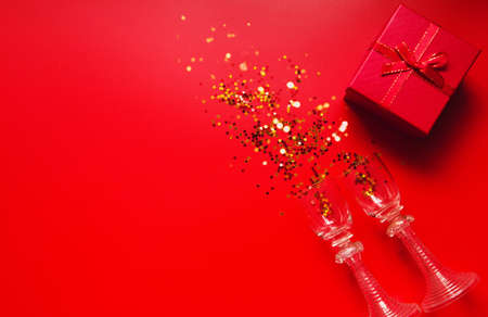 Red background with decorative metallic stars, two vintage glasses and red gift box. Holiday theme backdrop. Festive and party concept. Invitation card themeの写真素材