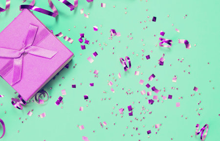 Present box on mint background with shiny confetti. Holiday and festive backdrop. Flat lay style....