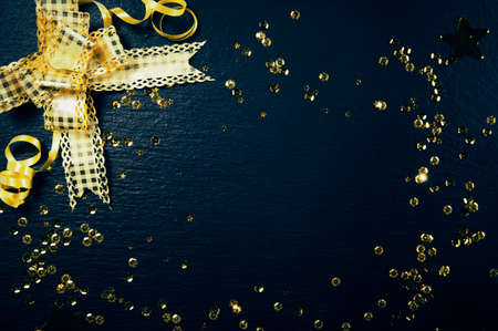 Big golden decorative bow and sequins on black background. Christmas or birthday backdrop. Celebration and party concept. Flat lay style. Image is with copy spaceの写真素材