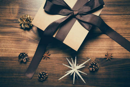 Present paper box wrapped with brown ribbon on wooden background with pine cones. Celebration and holiday concept. Christmas gift. Top view.の写真素材