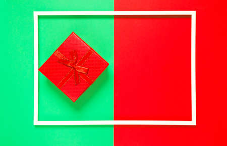 Composition with red present box on red and green background with white frame. Festive and  holiday concept. Top view. Copy spaceの写真素材