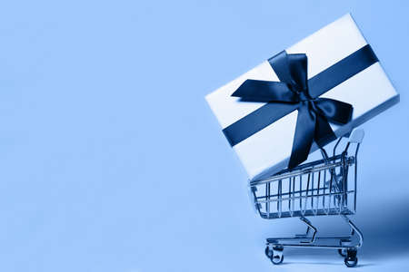 Small decorative trolley with present box on bright colorful background. Christmas or birthday gift. Sales and shopping concept.  Image is with copy space. Color 2020 inspiredの写真素材