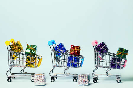 Small decorative trolleys with present boxes on bright colorful background. Christmas or birthday gift. Sales and shopping concept.の写真素材