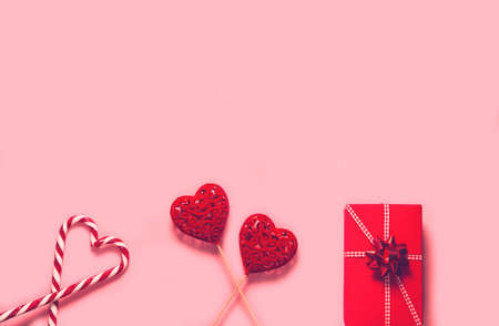 Abstract composition with two decorative hearts, lollipops and red present box on pink paper background. Valentine day theme. Love and romance concept. Flat lay. Top viewの写真素材