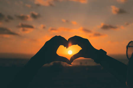 Girls hands in heart shape with sun light and colorful sky on the beach as a background. Love concept.の写真素材