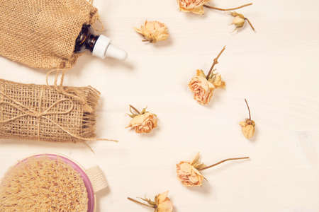 Set of natural soap, aroma oil and body brush with dried rose buds as a decoration on wooden background. Home spa concept. Beauty rituals theme.の写真素材