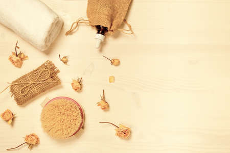 Set of natural soap, aroma oil, white towel and body brush with dried rose buds as a decoration on wooden background. Home spa concept. Beauty rituals theme.の写真素材