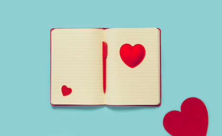 Notepad with pen and red decorative hearts on blue background. Valentine's day concept. Love and romance theme. Flat lay. Top viewの写真素材