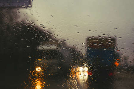 City road seen through rain drops on the car windshield. Focus is on some water dropsの写真素材
