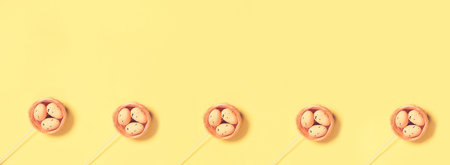 Decorative Easter eggs in nest on yellow background. Copy space. Top view