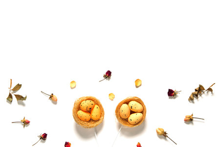 Decorative Easter eggs in nest on white background with dried rose flowers. Copy space. Top view