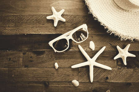 Summer composition with sunglasses, straw hat, starfishes and shells on wooden table. Vacation and travel concept. Sepia toned effectの写真素材