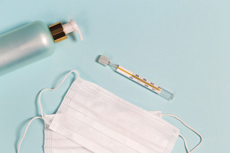 Medical masks, hand sanitizer gel and thermometer on pastel blue background. Coronavirus protection...