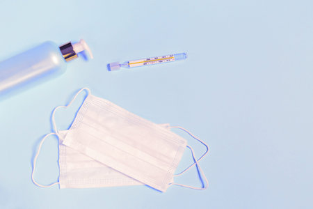 Medical masks, hand sanitizer gel and thermometer on pastel blue background. Coronavirus protection...