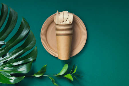 Eco friendly craft paper tableware on green background with monstera leaf. Recycling concept. Top view. Copy space. Zero waste theme.の写真素材