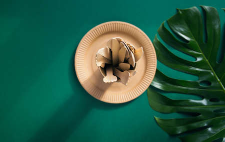 Eco friendly craft paper tableware on green background with monstera leaf. Recycling concept. Top view. Copy space. Zero waste theme.の写真素材