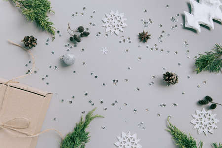 Craft present box on pastel background with juniper branch, pine cones, decorative fir tree, balls, silver snow flakes, stars and sequins. Christmas gift. Celebration and party concept. Flat lay. Top viewの写真素材