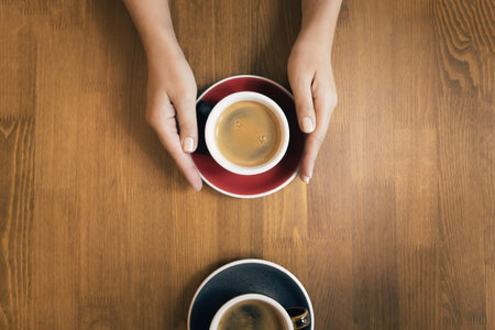 Female hands holding cup of coffee on wooden table as a background. Flat lay style. Top viewの写真素材